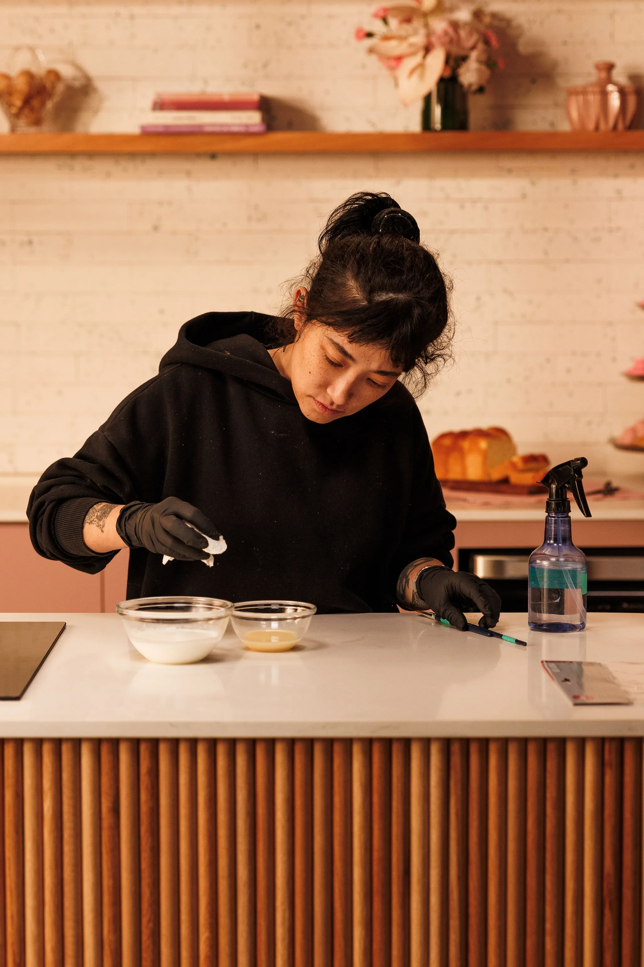 Gloved hands adjusting small test bowls on the counter, with a spray bottle beside them.
