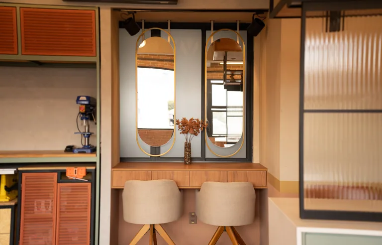 The dressing room counter with two oval gold mirrors, a wooden top and two beige chairs.