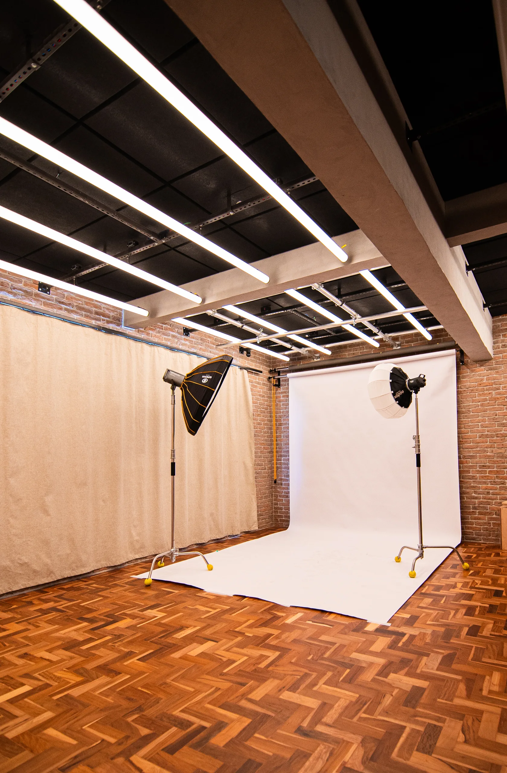 Fundo infinito branco montado no Loft, com dois refletores em pé, cortina blackout ao lado e parede de tijolo.